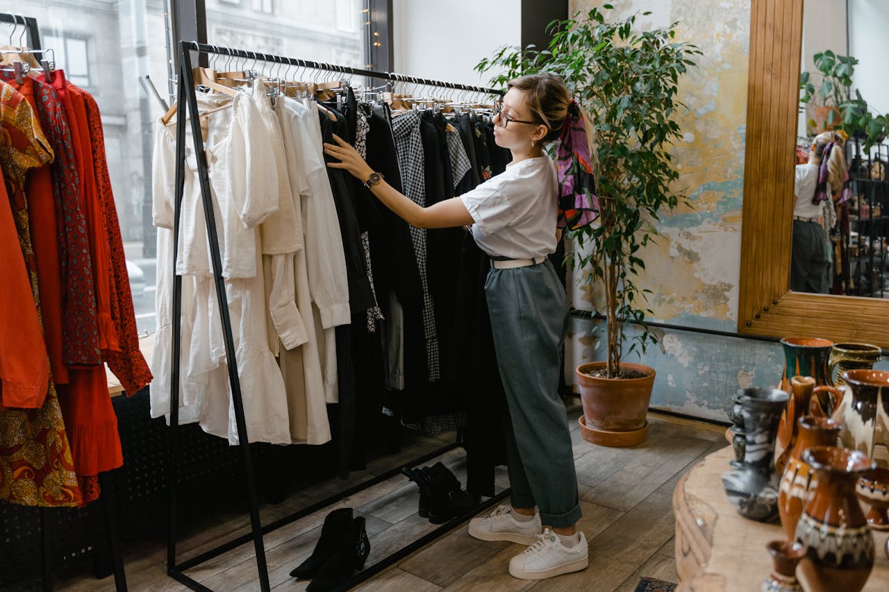 A stylish woman browsing clothes in a chic boutique store with ceramics and plants.